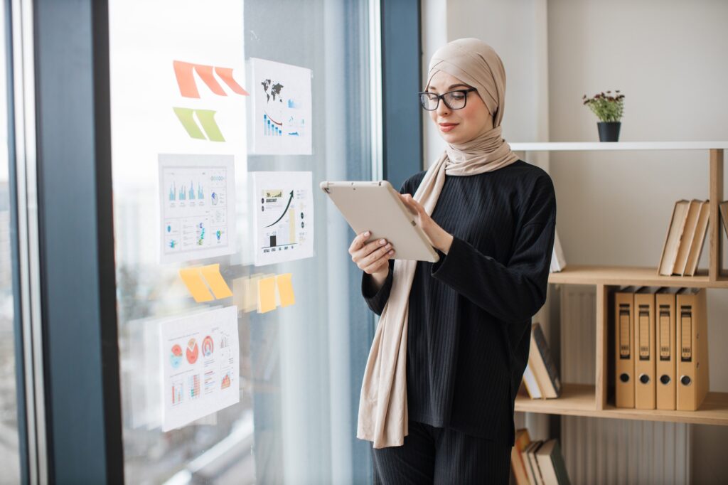 Manager with tablet standing near window with infographics